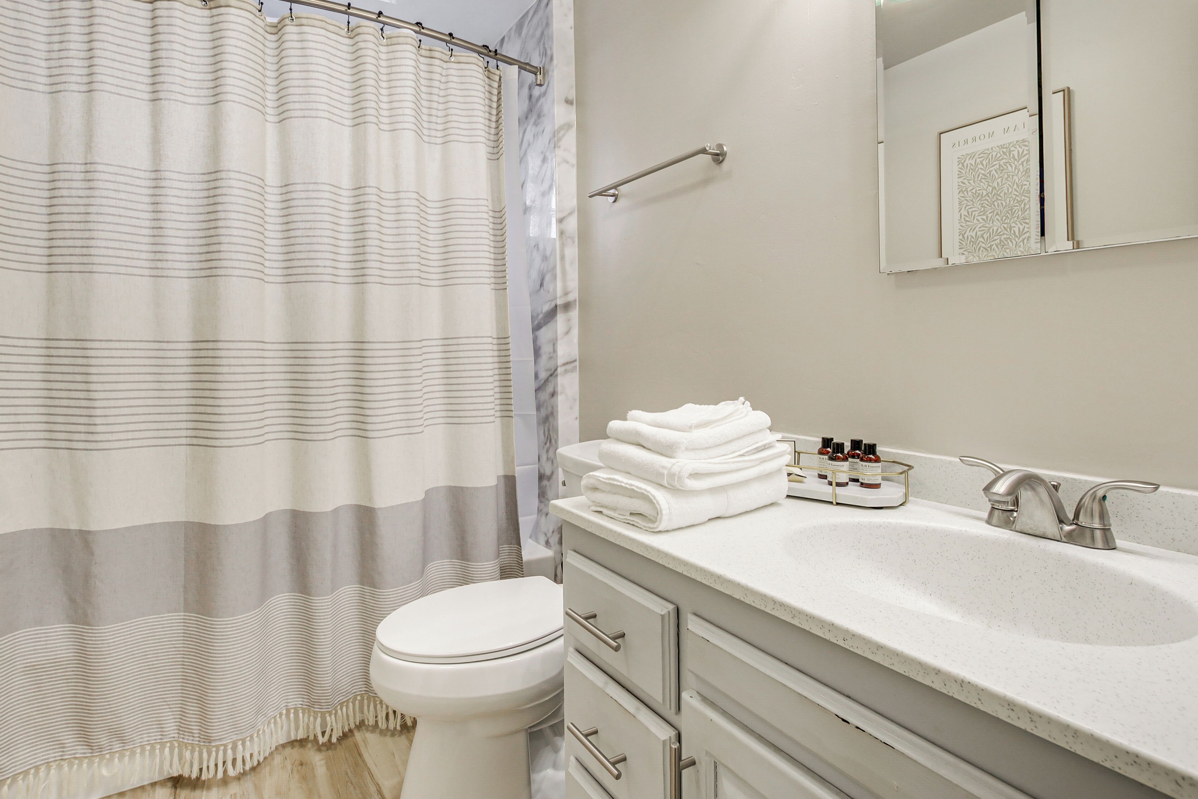 A bathroom with a striped shower curtain, a toilet, a sink with a towel rack, and a mirror.
