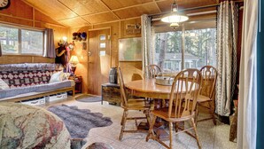 Ein gemütliches Blockhaus-Interieur mit einem Holzespeisetisch, Stühlen, einer Couch und einem großen Fenster.