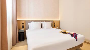 A hotel room with a large bed, a bedside table with a lamp, and a wall-mounted speaker.