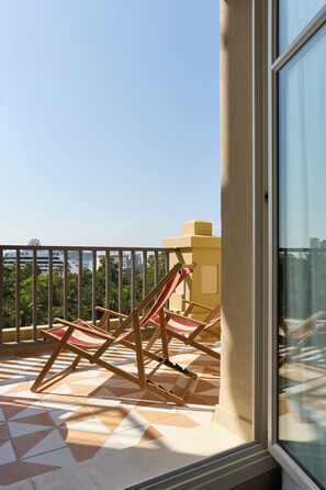 Een balkon met betegelde vloer en twee houten lounge stoelen.