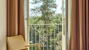 Een kamer met een bed, gordijnen, een stoel en een balkon met een hekwerk.
