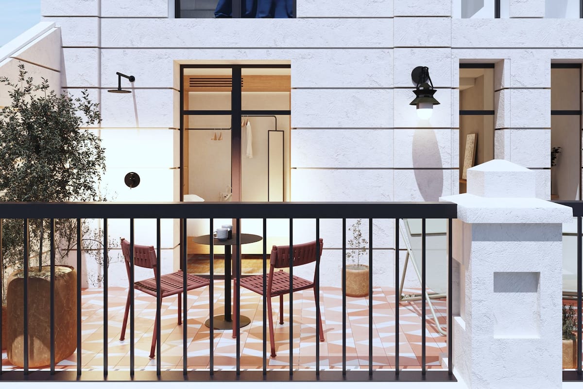 A modern building with a balcony featuring a table and two chairs, a white textured wall, and a door leading inside.