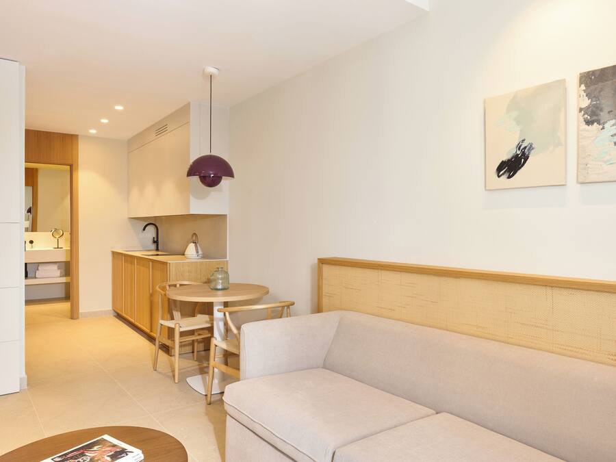 A modern living room with a sofa, a dining table with chairs, a kitchen area, and artwork on the wall.