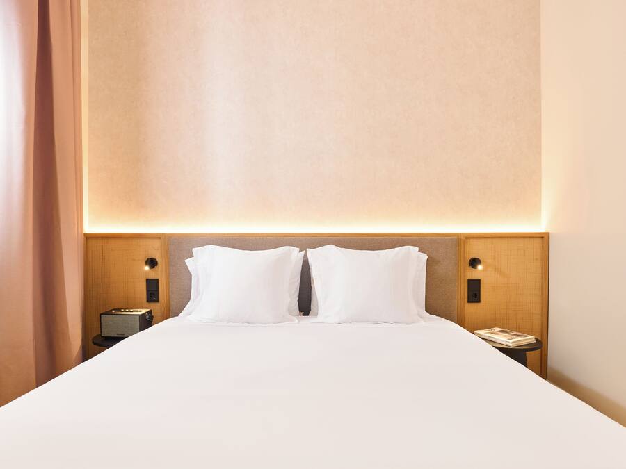 A hotel room with a large bed, two bedside tables, and a headboard with integrated lighting.