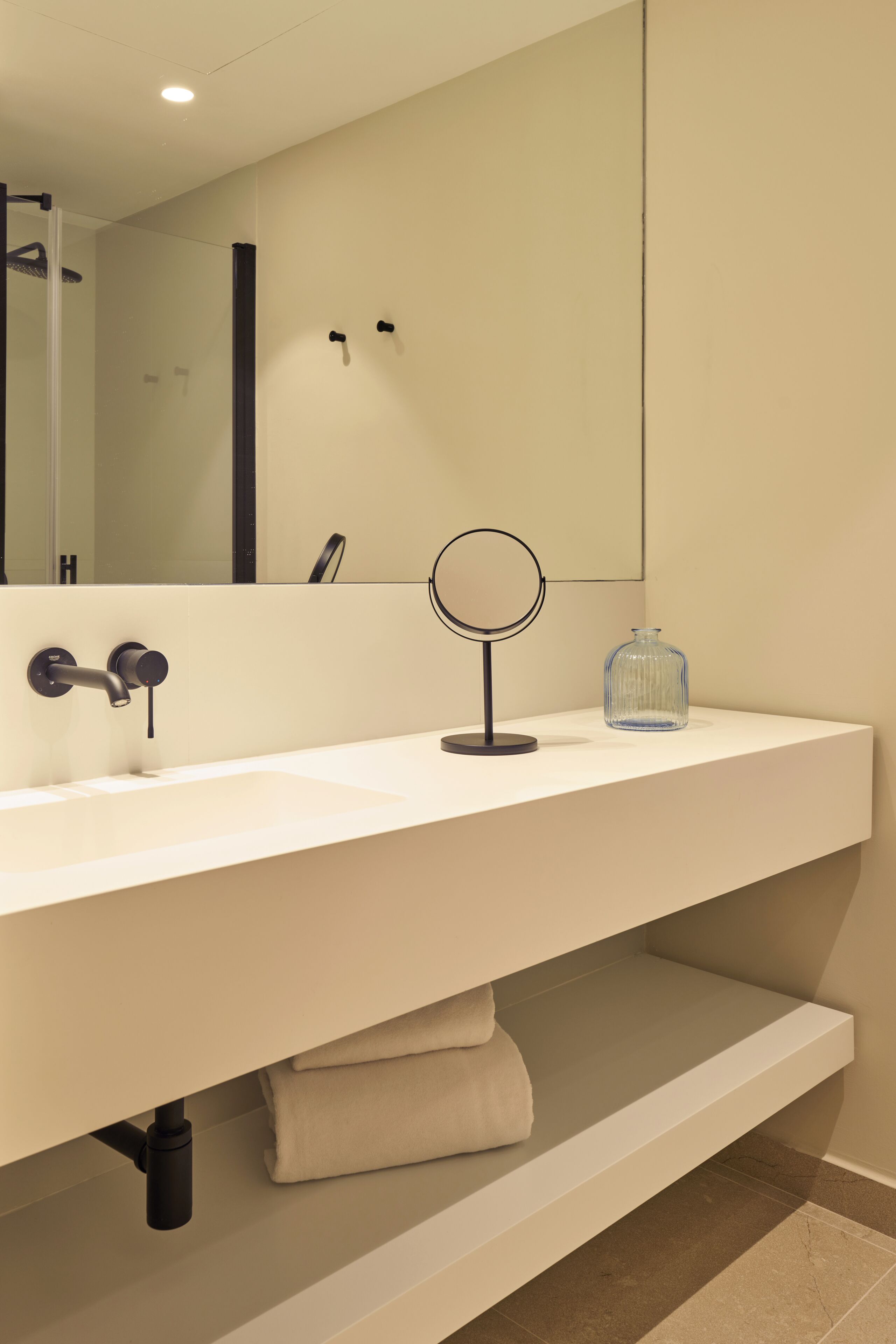 A modern bathroom with a large mirror, a round mirror, and a glass vase on the sink.