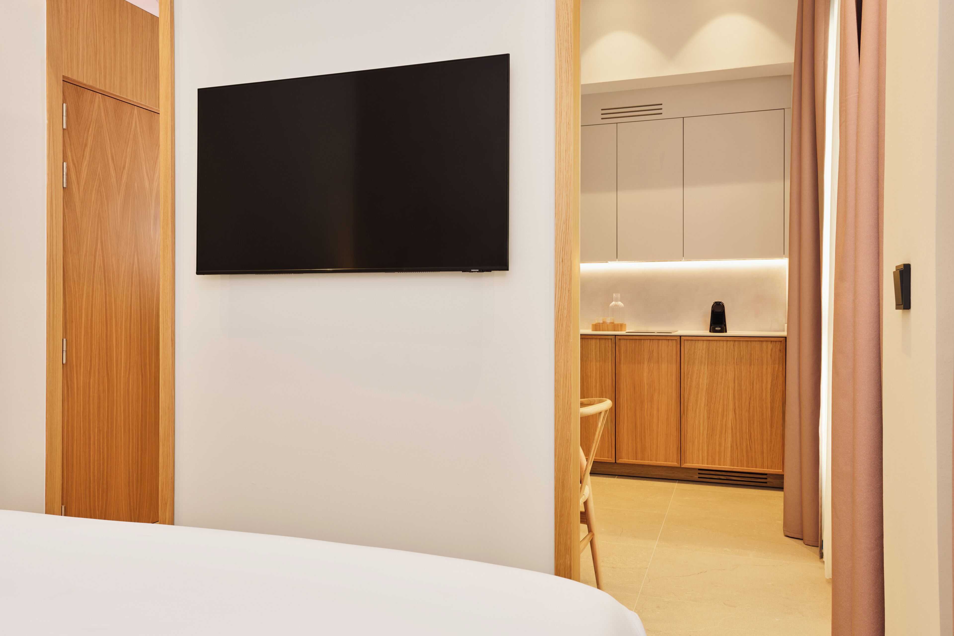 Une chambre d’hôtel équipée d’un lit, d’un téléviseur à écran plat fixé au mur, d’armoires en bois et d’un coin cuisine.