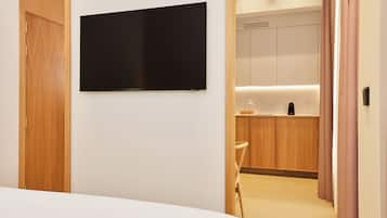 Hotellihuone, jossa on sänky, seinälle asennettu taulutelevisio, puukaapit ja pieni keittotila.