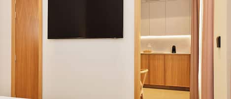 Habitación de hotel con cama, televisor de pantalla plana en la pared, muebles de madera y una zona de kitchenette.