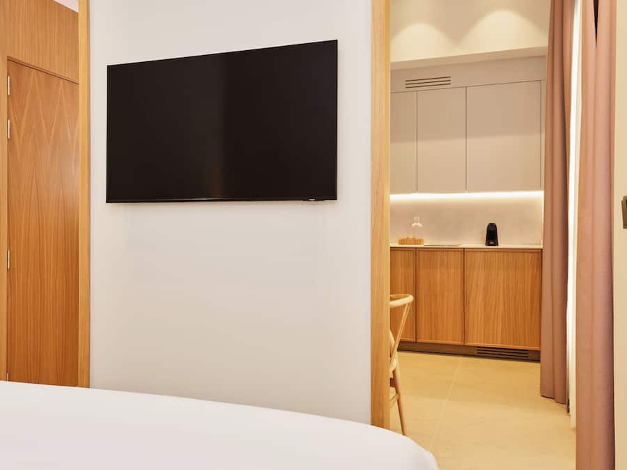 Habitación de hotel con cama, televisor de pantalla plana en la pared, muebles de madera y una zona de kitchenette.