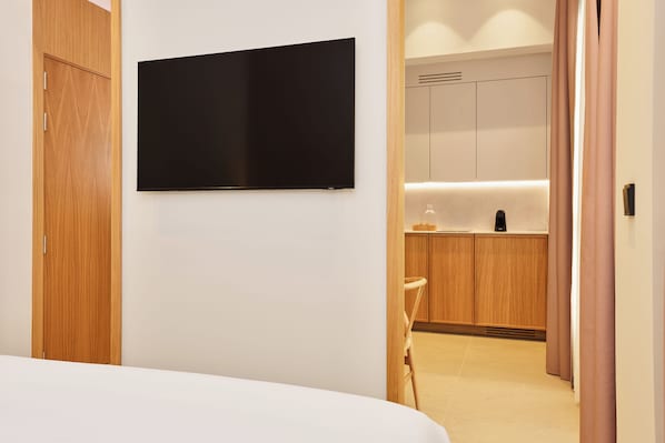 A hotel room with a bed, a flat-screen TV mounted on the wall, wooden cabinets, and a kitchenette area. - Ocean Drive Málaga (Málaga)
