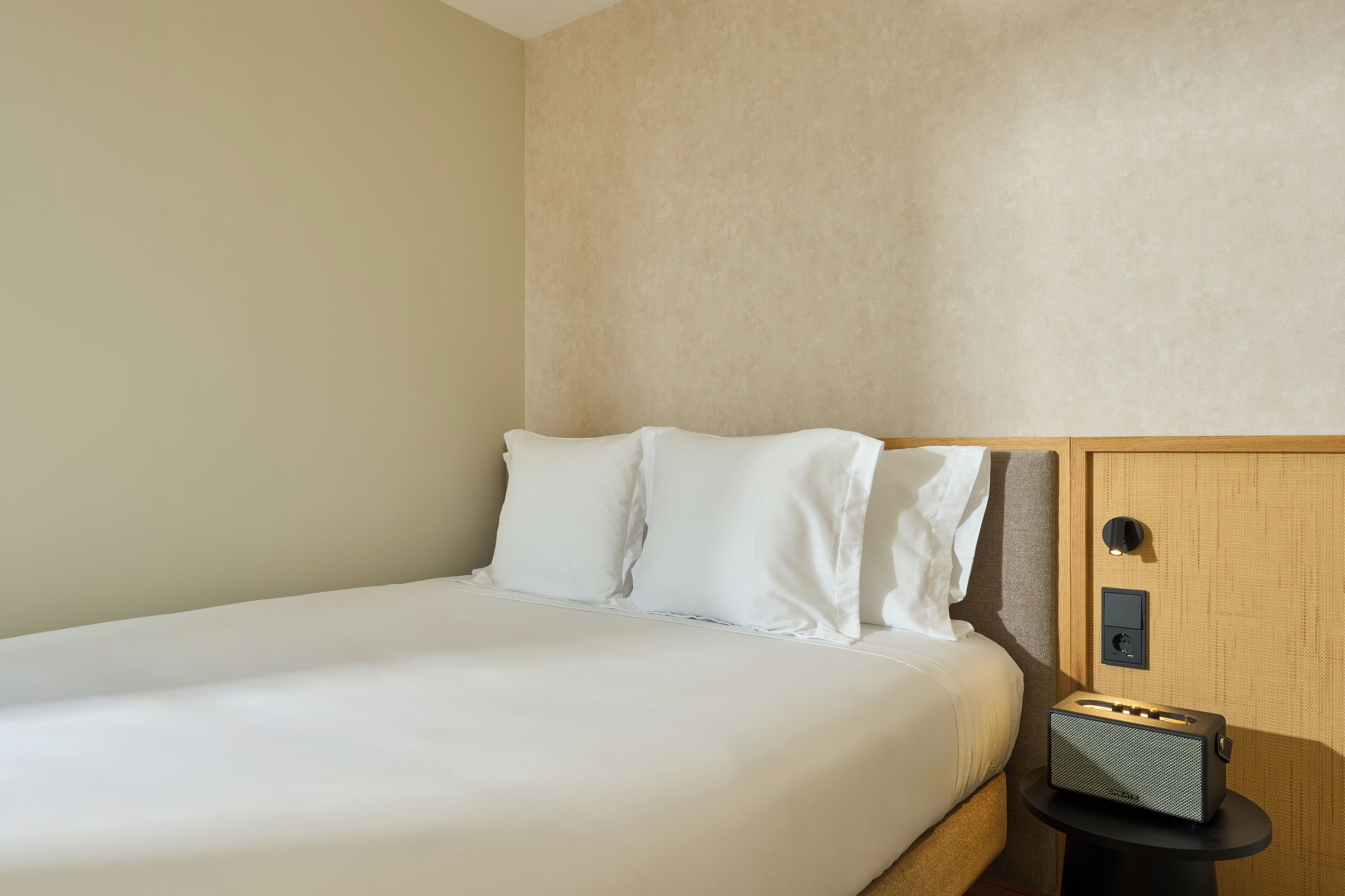 Habitación de hotel con cama, mesita de noche y panel de control en la pared.
