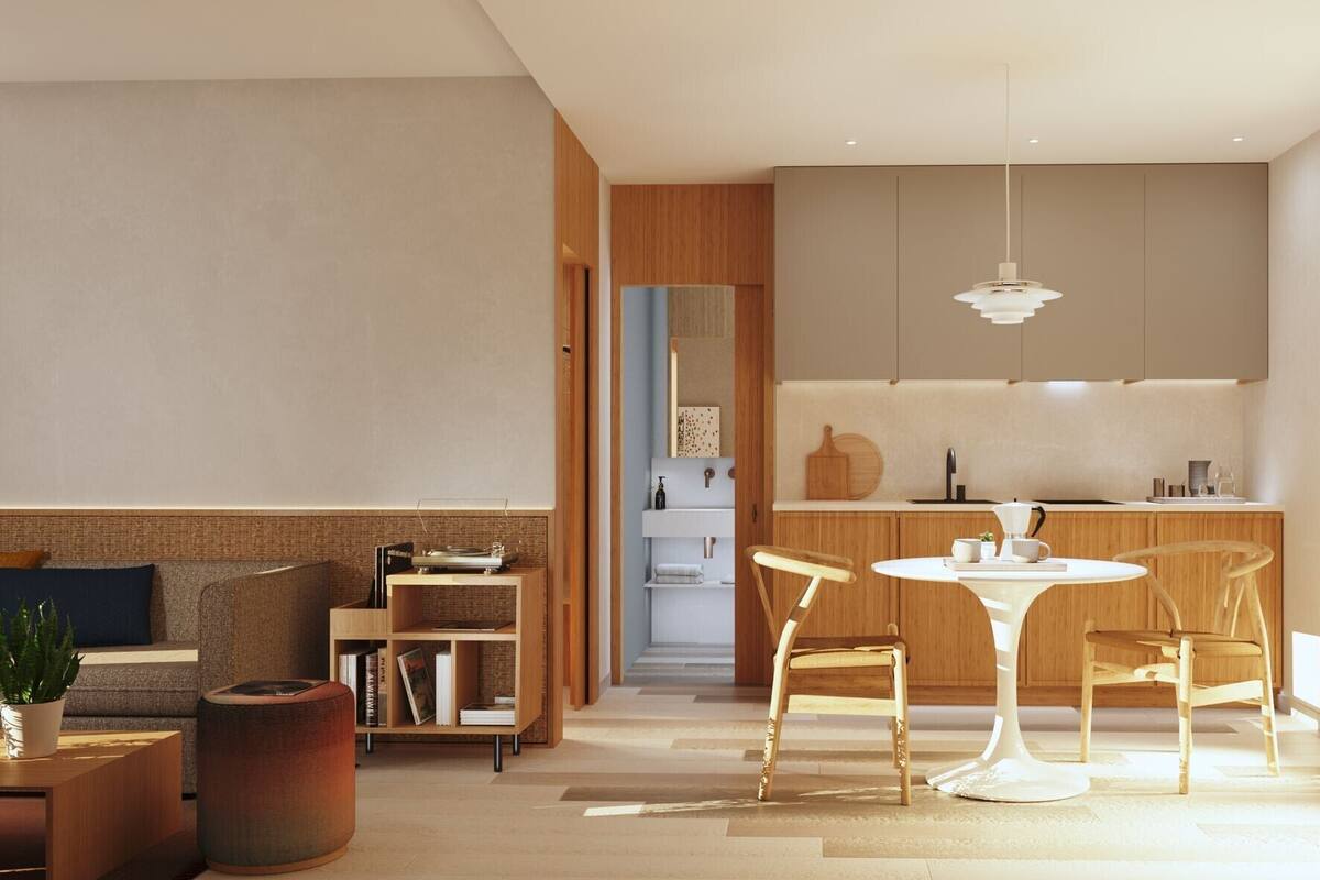 A modern living room with a sofa, a coffee table, and a bookshelf. There is a dining area with a table and chairs. The kitchen has wooden cabinets and a hanging light fixture.