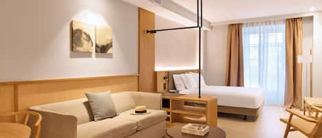 Quarto de hotel com sofá, mesa redonda pequena, cama e mesa de cabeceira.