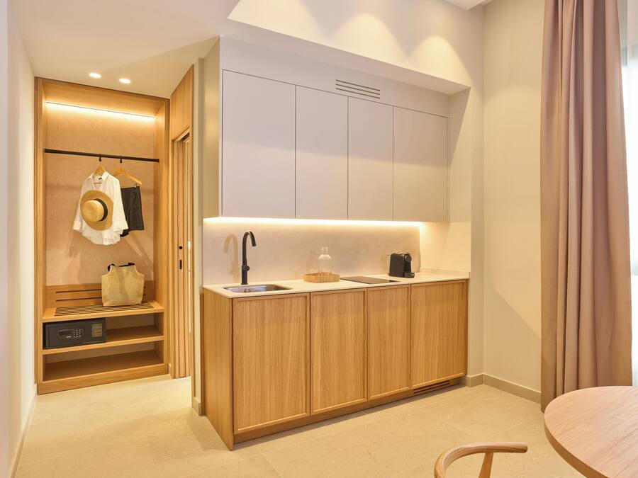 Una habitación de hotel moderna con una kitchenette de madera, un armario empotrado y un área de descanso.
