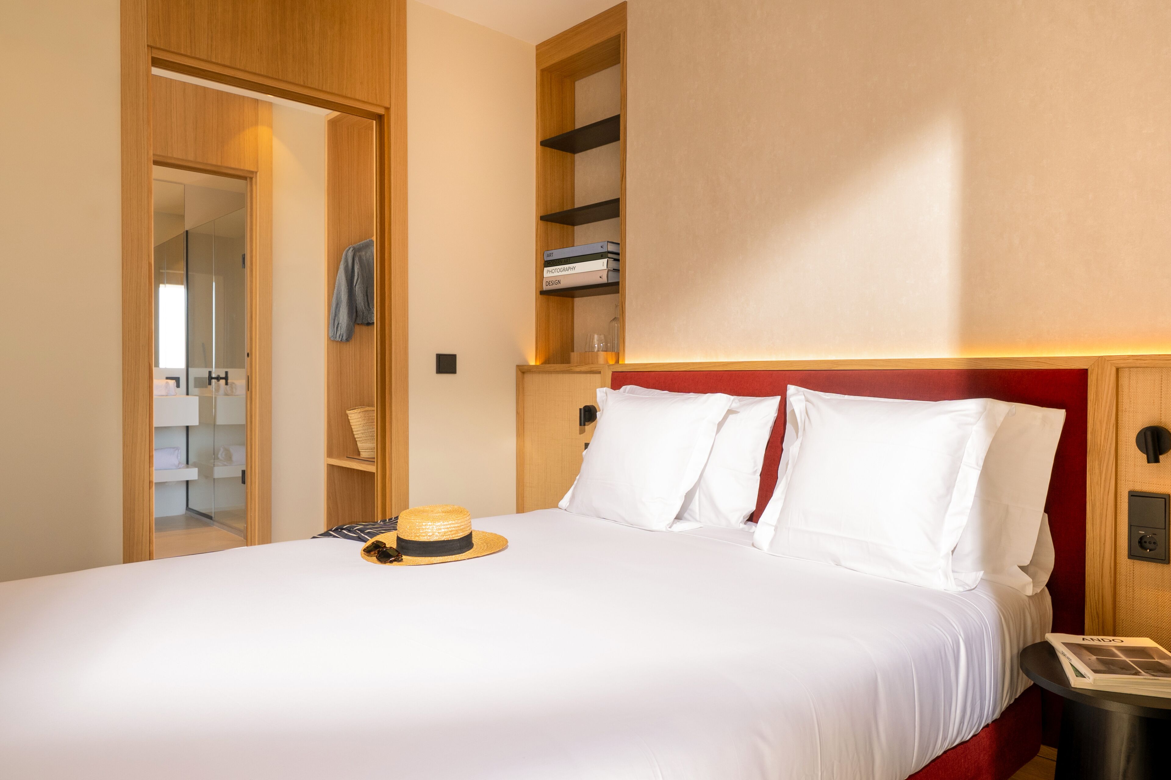 Habitación de hotel con cama, mesita de noche, armario y una estantería con libros.