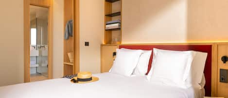 Habitación de hotel con cama, mesita de noche, armario y una estantería con libros.