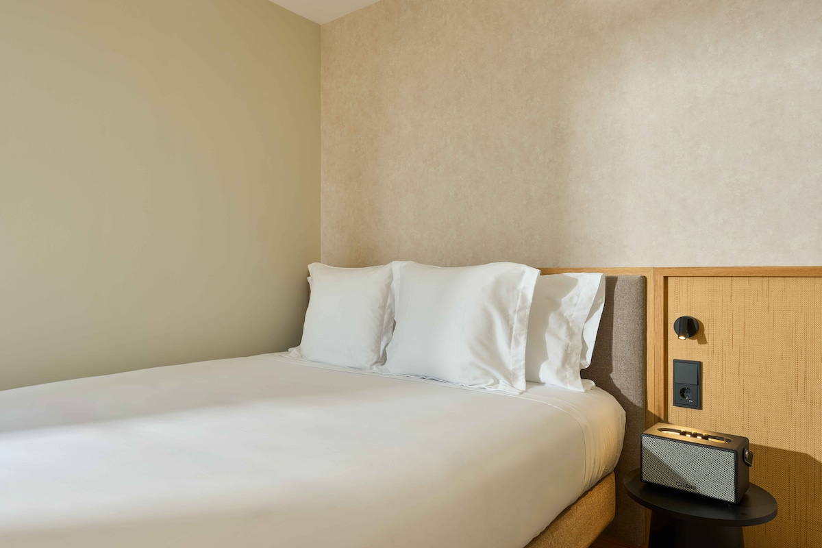 A single bed with white bedding in a room with beige walls and a wooden headboard.