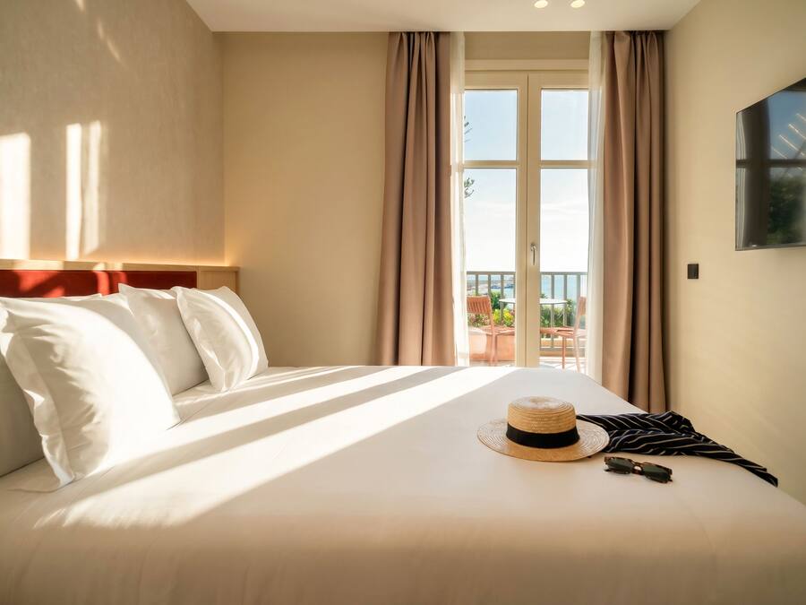 Une chambre d’hôtel avec un lit, une vue sur l’extérieur et un chapeau posé sur le lit.