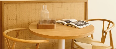 Une table ronde en bois, accompagnée de deux chaises en osier, d’une bouteille en verre et d’un magazine.