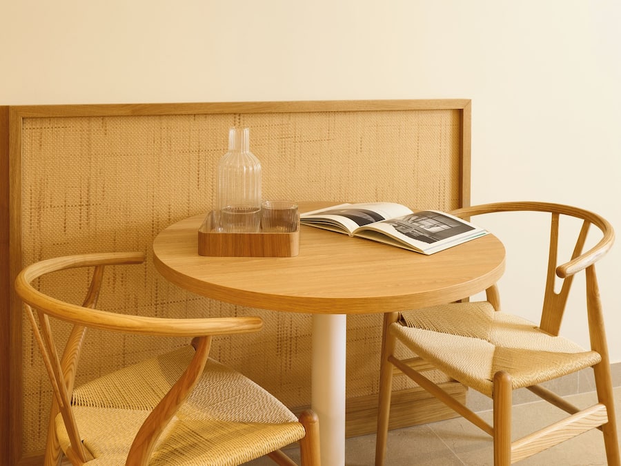 Una mesa redonda de madera con dos sillas de mimbre, una botella de vidrio y una revista.