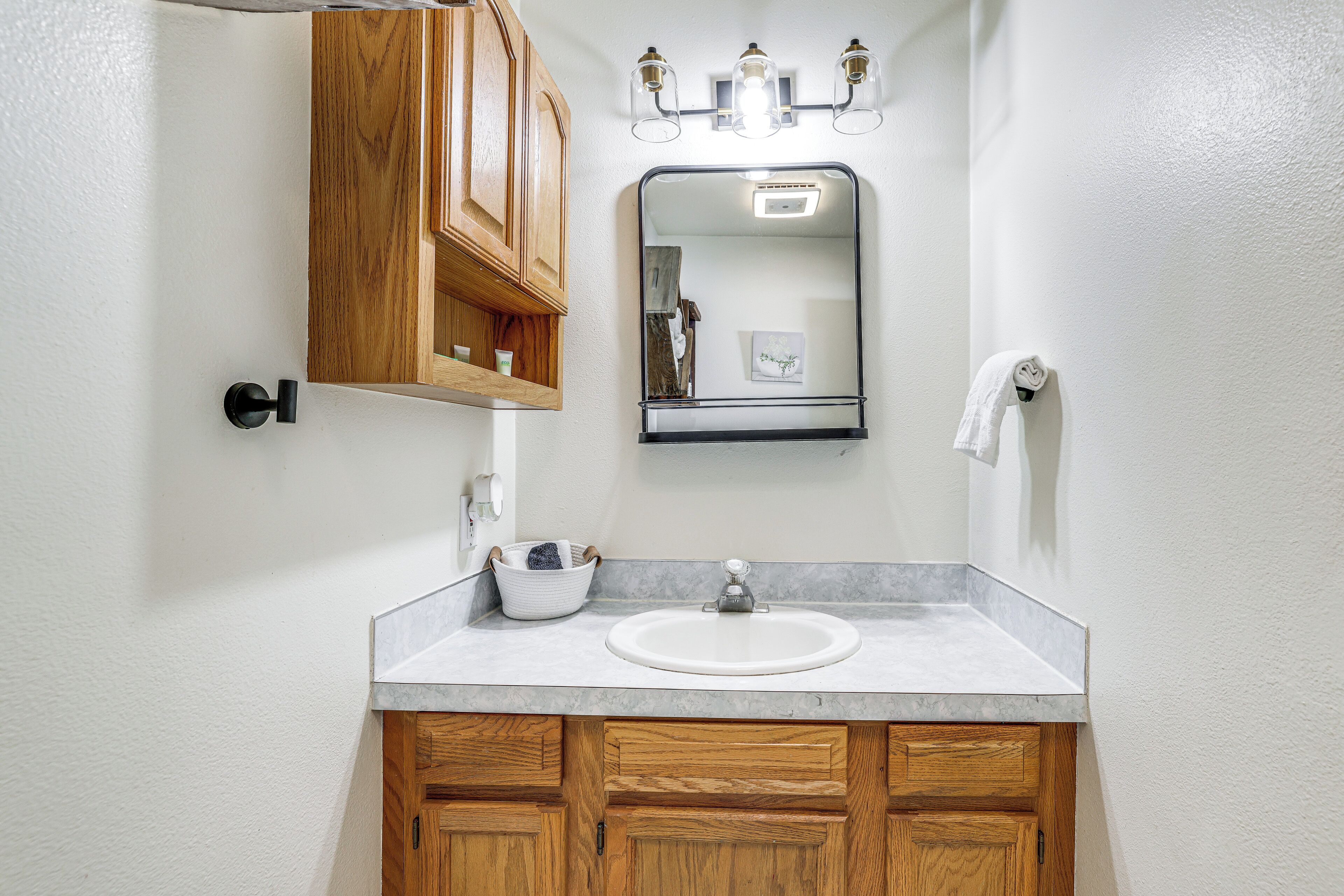 A bathroom with a white sink, wooden cabinets, a mirror, and a towel hanging on the wall.