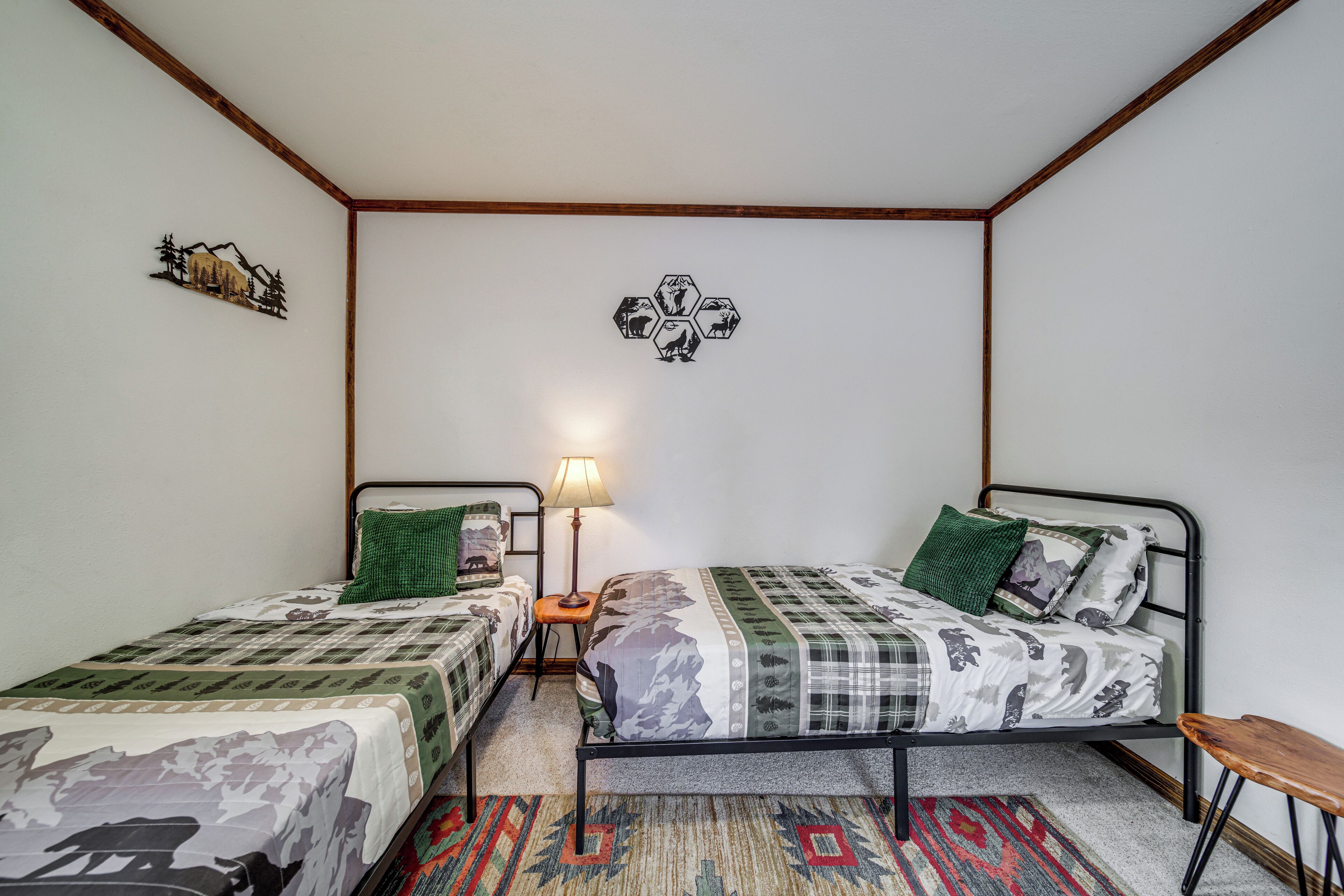 A room with two single beds, a nightstand with a lamp, a rug, and a wall decoration.
