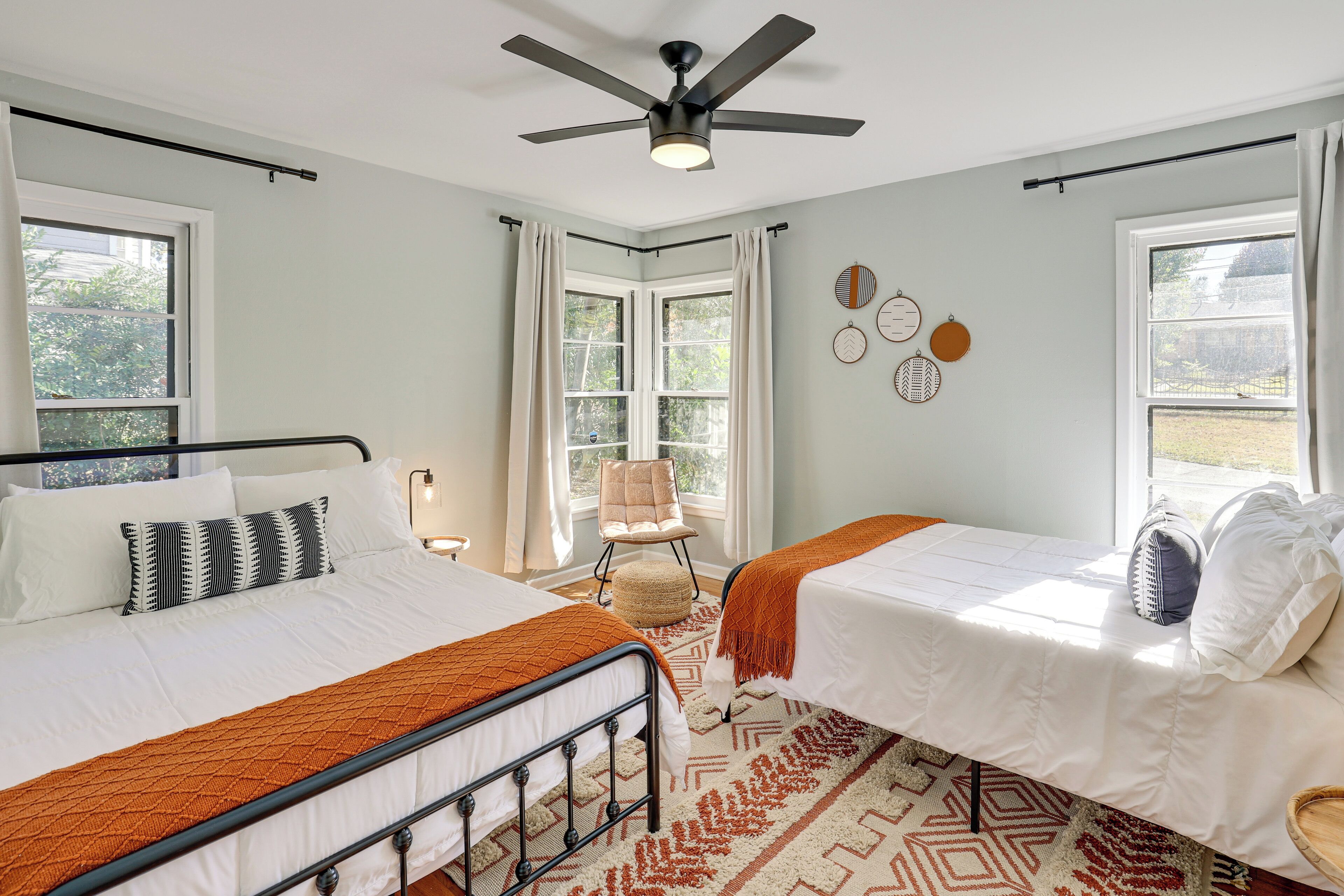 Une chambre avec deux lits, un ventilateur de plafond et de grandes fenêtres.