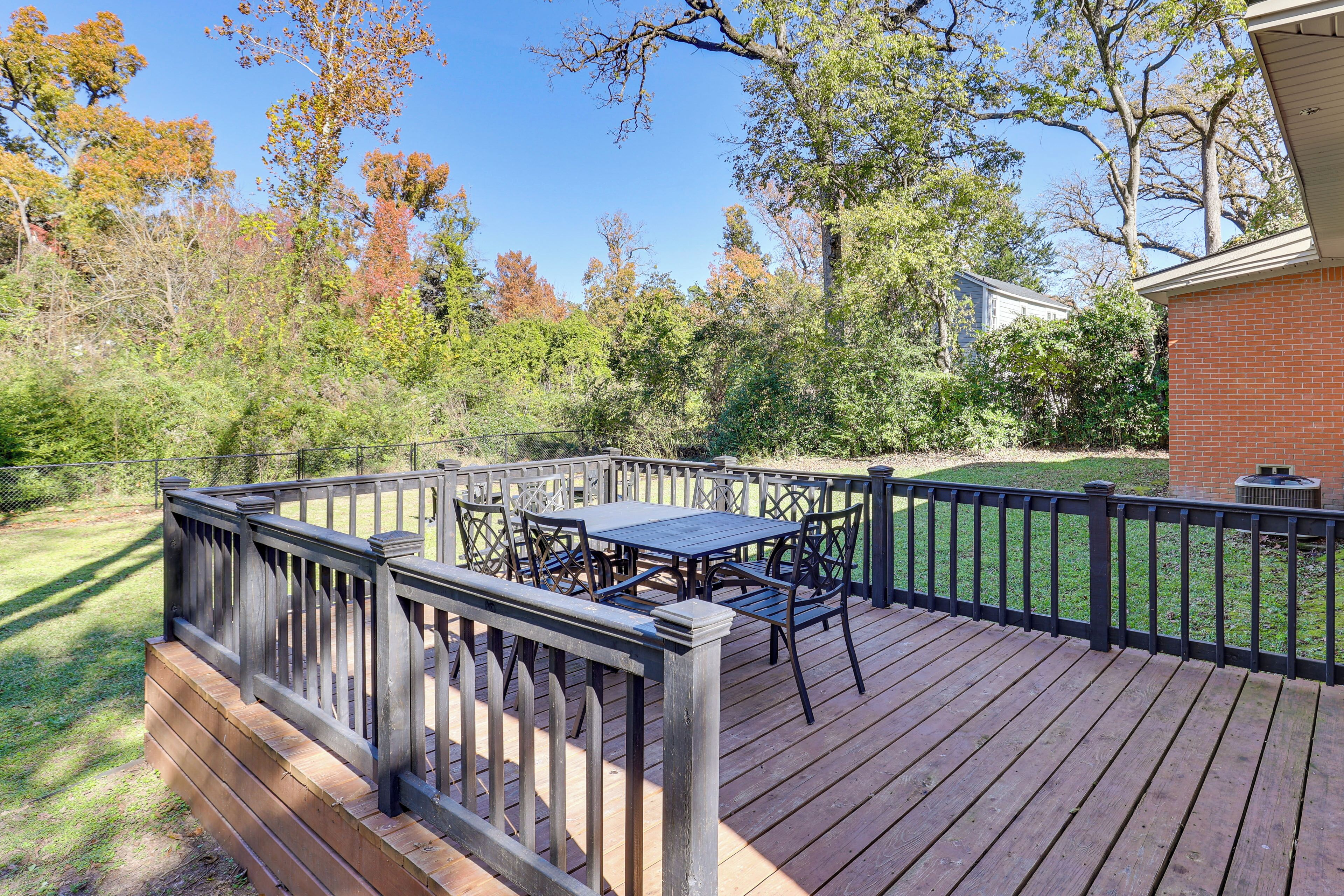 Une terrasse en bois avec une table et des chaises, entourée d’une clôture et d’arbres.