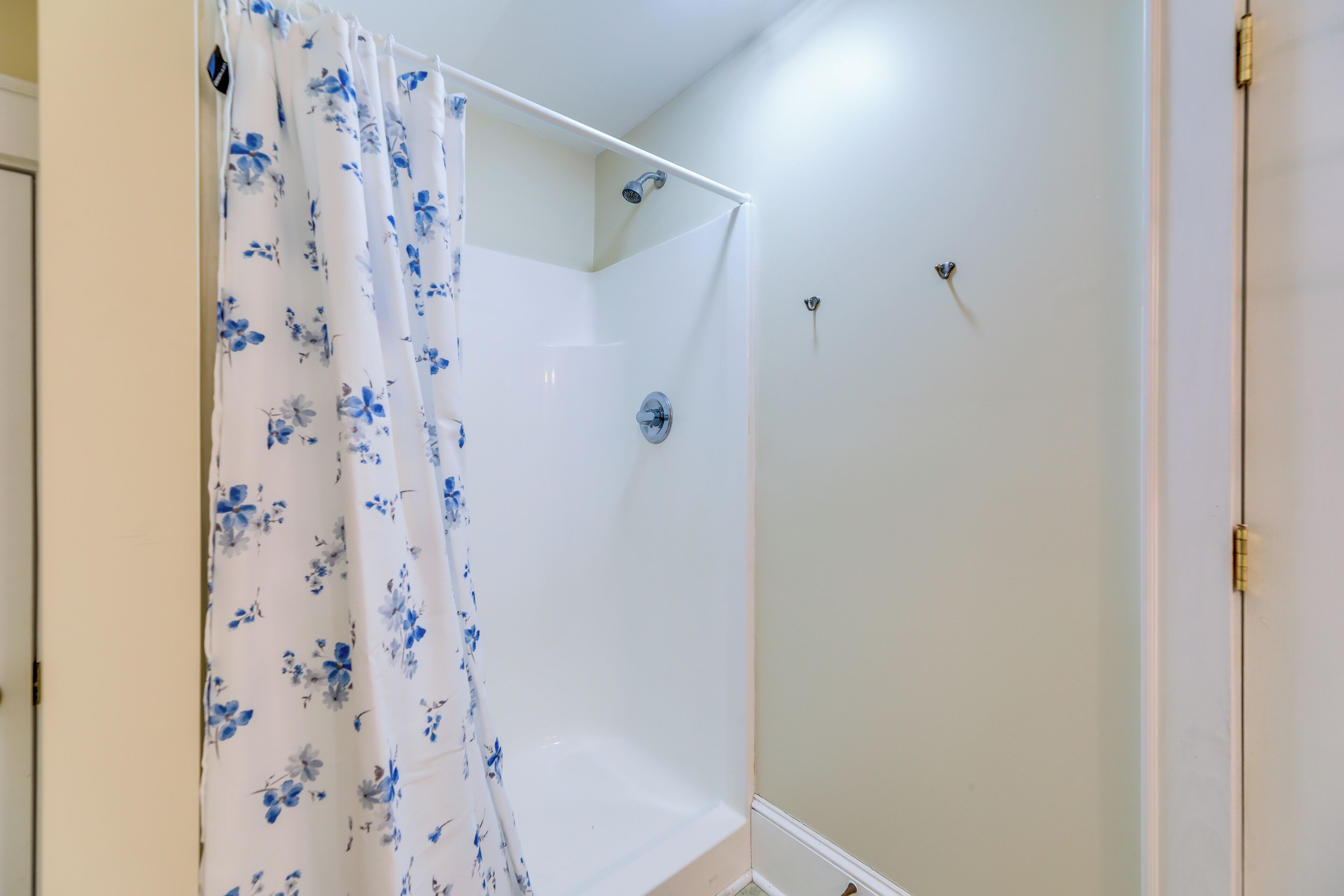 A shower area with a white shower curtain featuring blue floral patterns.