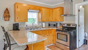 A kitchen with wooden cabinets, a granite countertop, a built-in microwave, a stainless steel stove, and a window with a view of greenery. - Hike, Swim & Fish On-site: Blue Ridge Mtn Getaway (Thurmond)