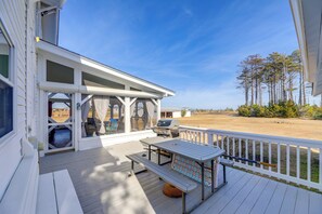 Una veranda coperta con tavolo e sedie, un barbecue e vista sulla spiaggia e sugli alberi.