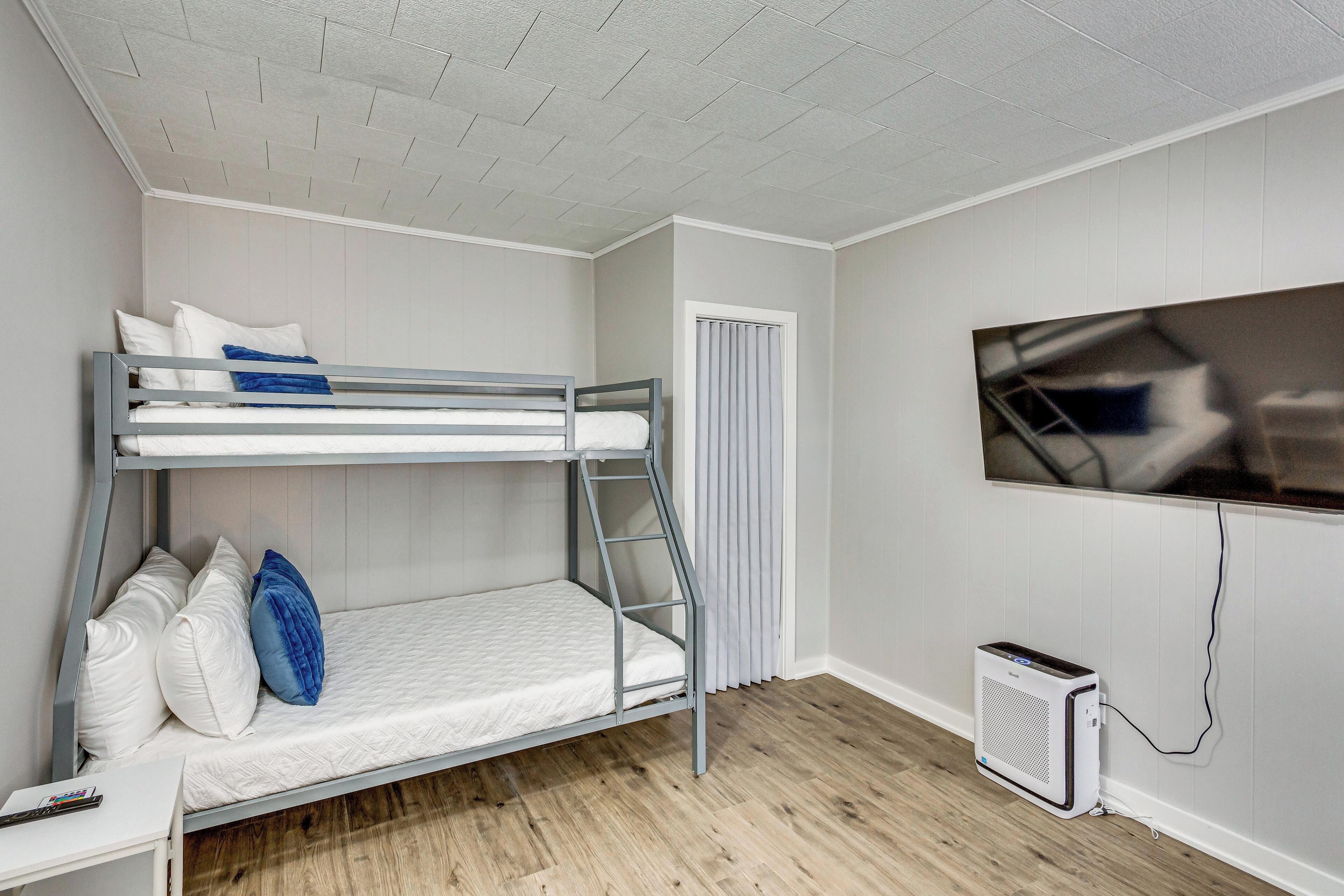 Una cama litera con escalera, un escritorio pequeño y un televisor montado en la pared.
