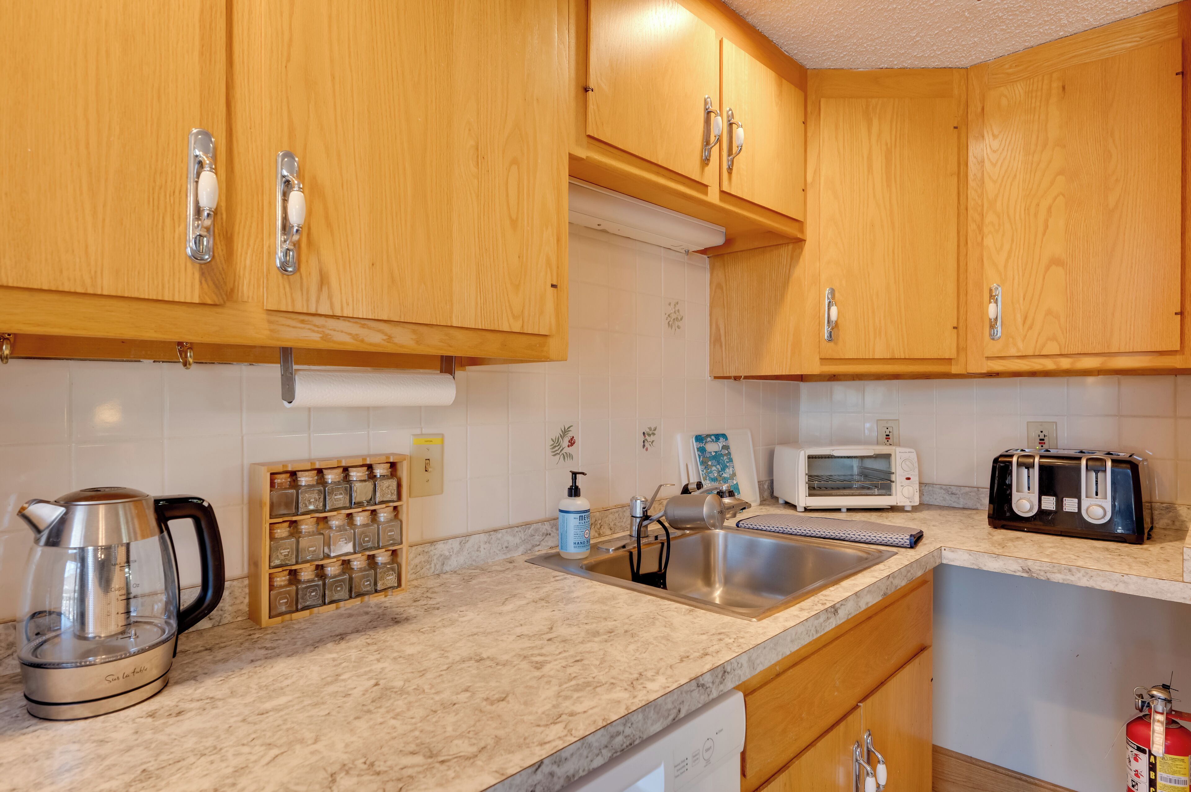 A kitchen with wooden cabinets, a stainless steel sink, a kettle, a toaster, and a microwave.