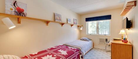 Un dormitorio con cama, escritorio, silla, ventana y estanterías fijas a la pared.