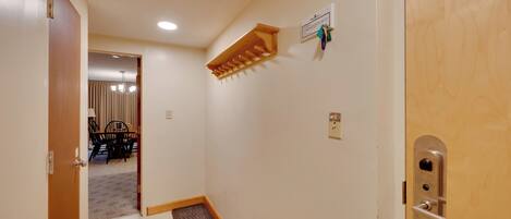 Un pasillo con una puerta de madera, un equipo de aire acondicionado instalado en la pared, un timbre y un felpudo en la entrada.