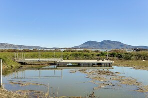 A calm water body with a dock and a bridge, surrounded by grassy areas and mountains in the background. - Clear Lake Living! Pet-friendly Gem w/ Fenced Yard (Lakeport)