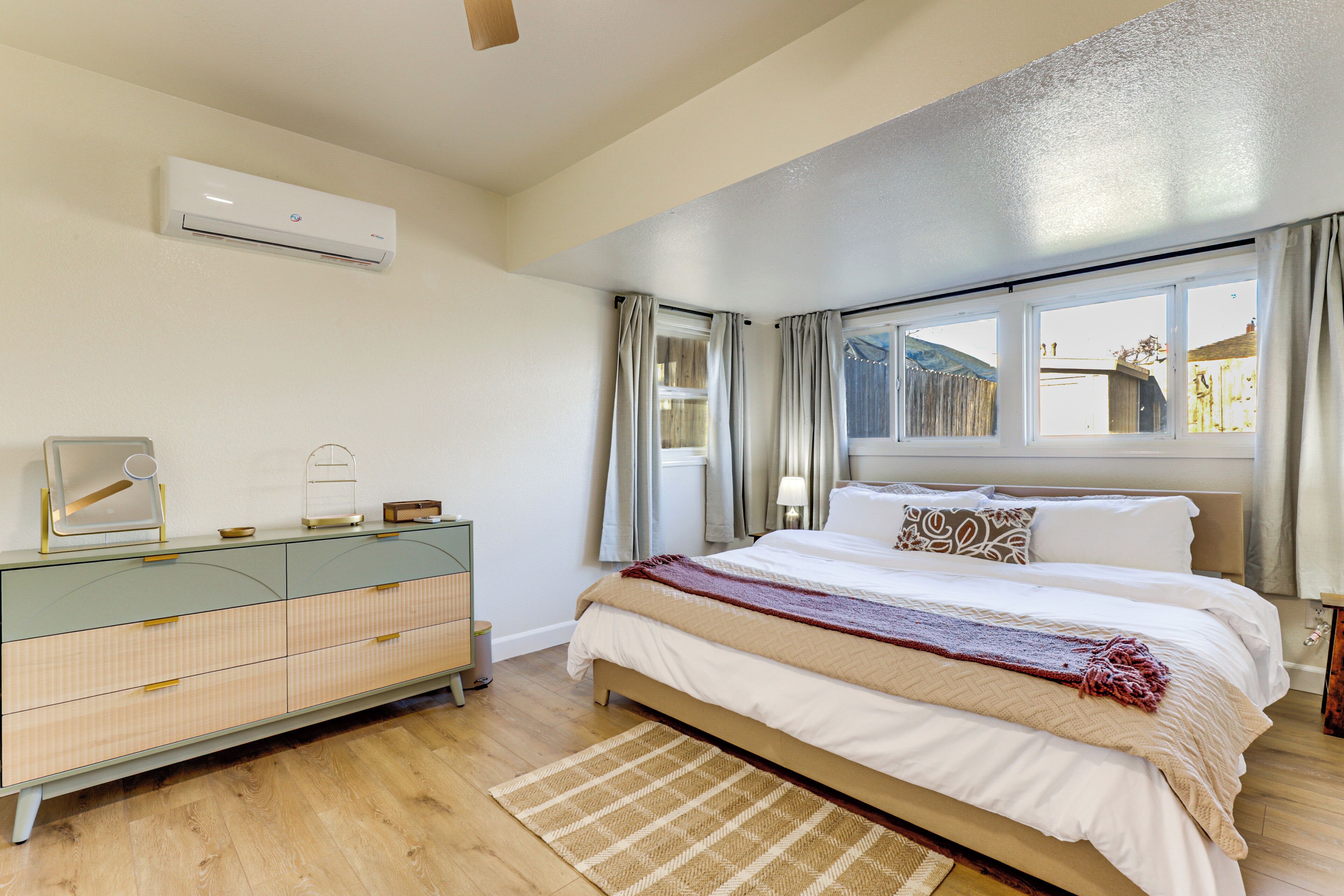 Un dormitorio con cama, cómoda, ventana con cortinas y un equipo de aire acondicionado.