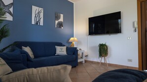 Ett vardagsrum med en blå soffa, ett litet sidobord med en lampa och en väggmonterad TV.