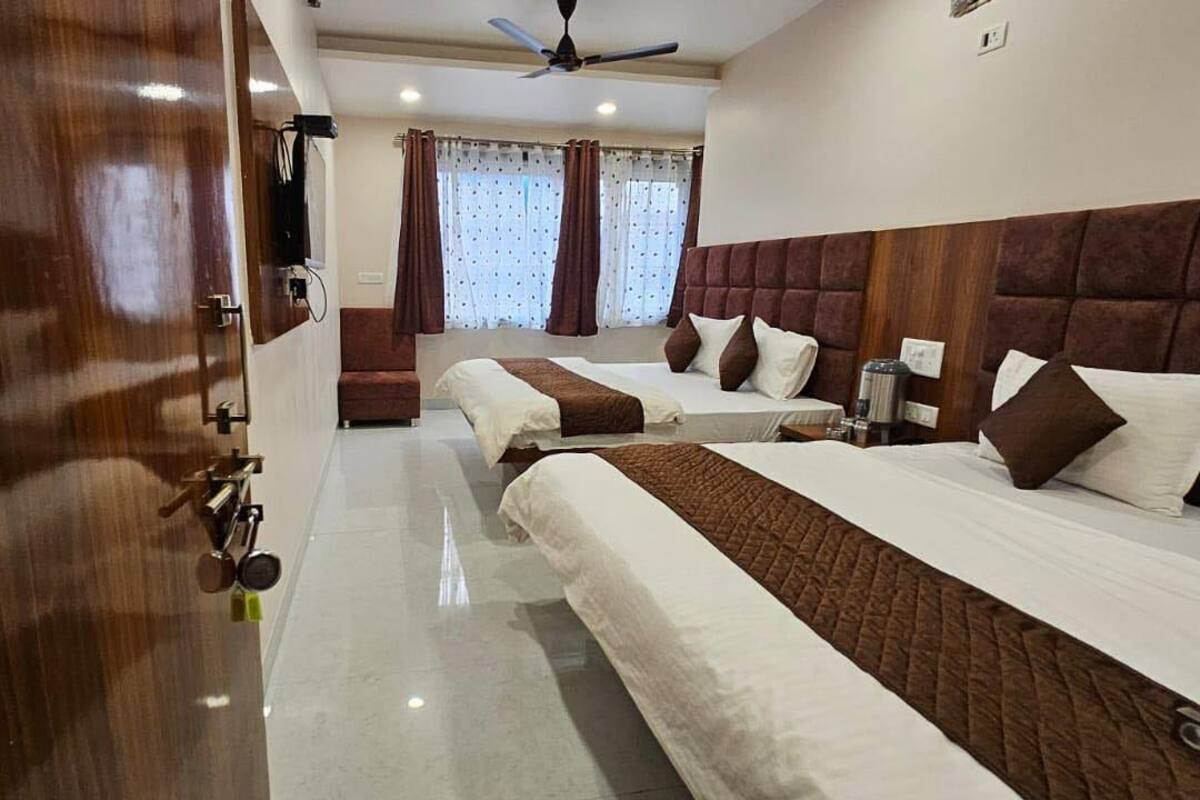 A hotel room with two beds, a wooden door, a ceiling fan, and a window with curtains.