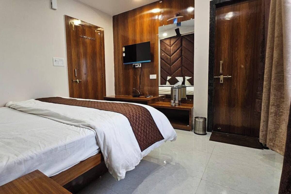 A hotel room with a bed, a wooden wardrobe, a television, and a mirror.