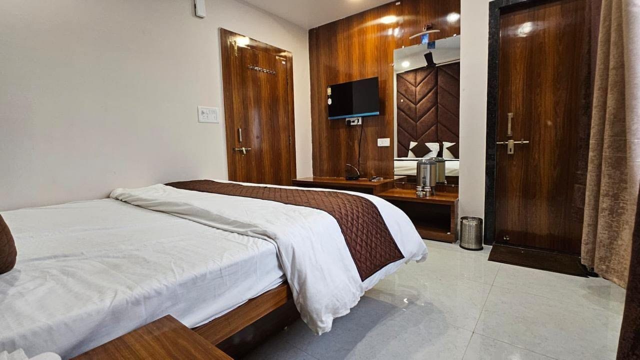 Una habitación de hotel con una cama, un televisor montado en un panel de madera y una puerta con espejo.