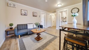 Una sala de estar moderna con un sofá azul oscuro, una mesa de centro de madera y un comedor con una mesa y sillas de madera.