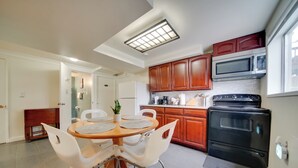 Una cocina moderna con armarios de madera, estufa negra, microondas y un comedor con una mesa redonda y sillas blancas.