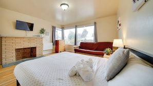 Habitación de hotel con una cama grande, chimenea, televisor montado en la pared y ventana con cortinas.