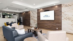 A modern living room with a sofa, armchairs, and a coffee table. A television screen displays a logo. - Gulf-front 2BR w/ Balcony: Suntide III - Unit 502 (South Padre Island)