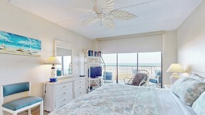 A bedroom with a bed, a desk, a chair, a bookshelf, and a balcony with a view. - Gulf-front 2BR w/ Balcony: Suntide III - Unit 502 (South Padre Island)