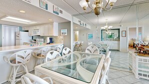 A spacious kitchen with white cabinetry, a central island with seating, and a dining area with a glass-top table and white chairs. - Gulf-front 2BR w/ Balcony: Suntide III - Unit 502 (South Padre Island)