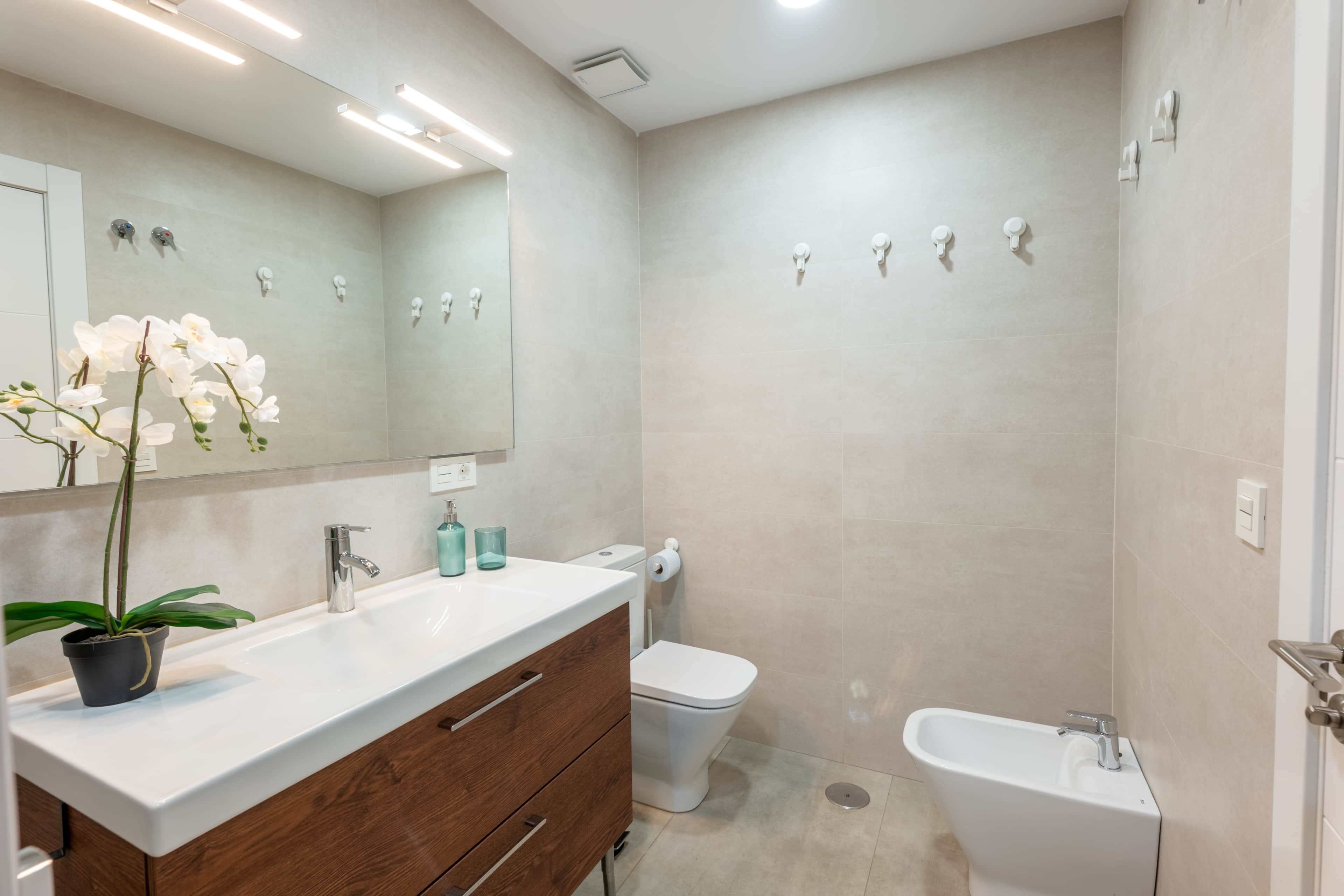 Un baño moderno con un lavamanos blanco, tocador de madera, inodoro y bañera.