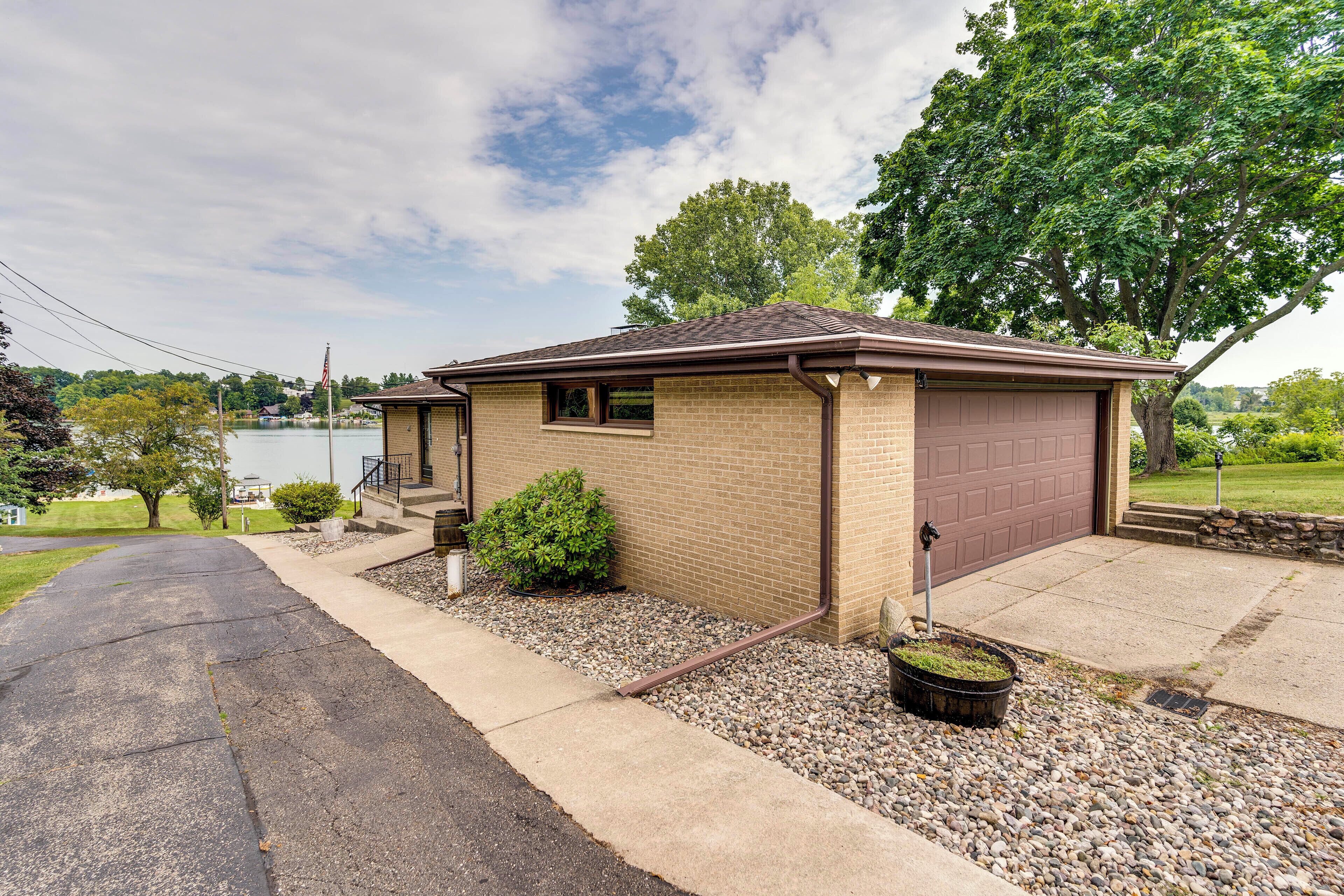 A single-story house with a garage, a small front yard with a gravel path, and a view of a lake.