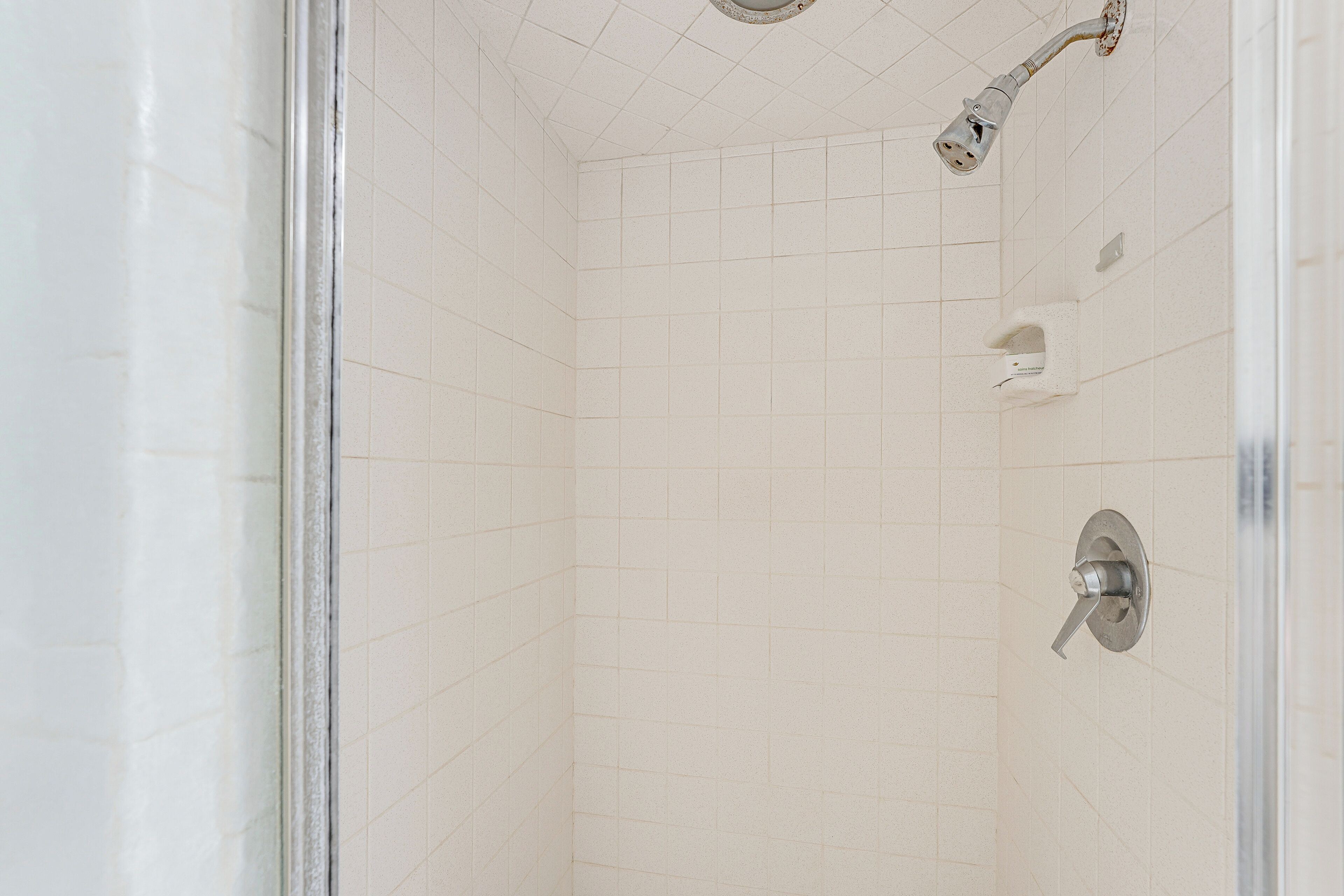 Un bagno con pareti piastrellate di bianco, una doccetta e un rubinetto.